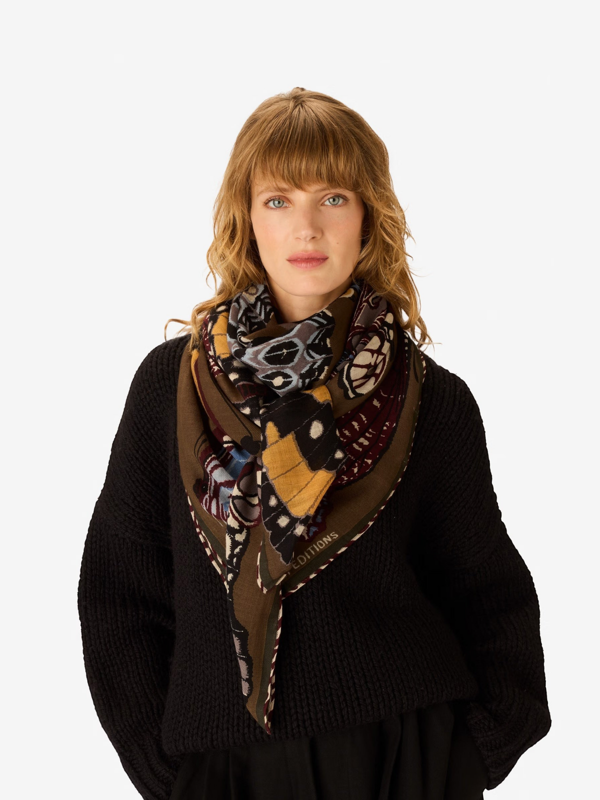The INOUI EDITIONS - PAPILLONS WOOL SCARF IN KHAKI by INOUI is a square scarf made in India, featuring an intricate and colorful butterfly pattern in brown, blue, yellow, and white hues on a tan background. Measuring 130 x 130 cm, it provides generous coverage and stylish versatility for any occasion.