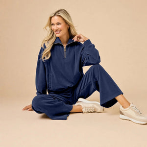 A woman seated on the floor wearing a Softies - Serenity 1/4 Zip Top with Wide Leg Pant lounge set in midnight, featuring a navy blue quarter-zip pullover and matching wide-leg lounge pants.