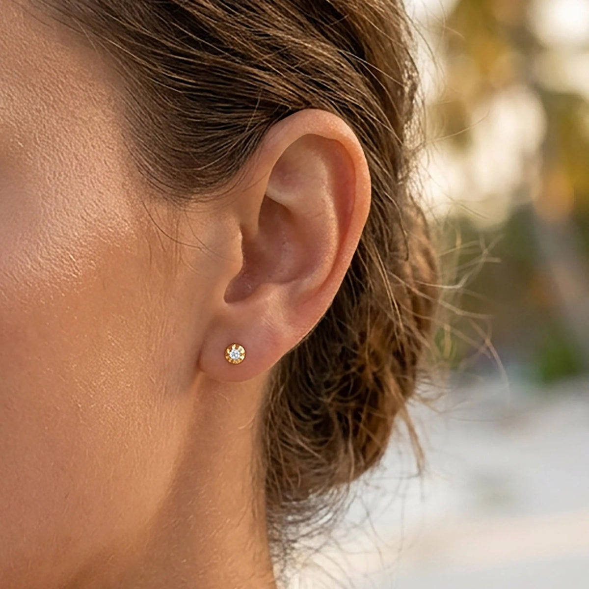 The ELLA STEIN - ALA STUD EARRINGS by ELLA STEIN are a pair of small gold stud earrings, each featuring a single round natural diamond set in a four-prong gold plated setting, displayed on a white background.