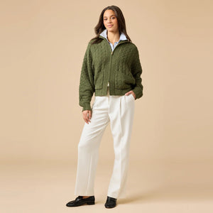 A woman wearing a cream-colored, plush SOFTIES - CABLE KNIT MARSHMALLOW FUNNEL NECK DOUBLE ZIP JACKET with a funnel neck and double zipper, paired with blue jeans.