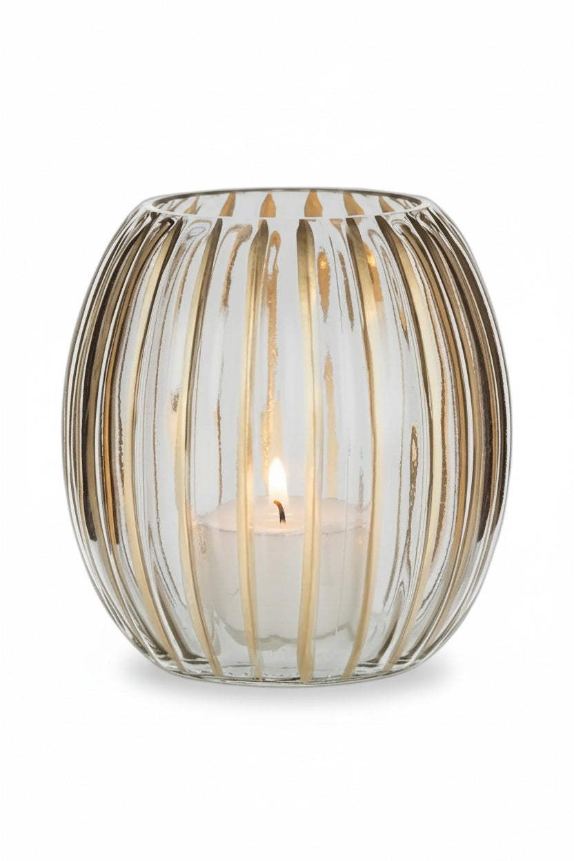 A lit tea light candle inside an ABBOTT RIBBED VOTIVE HOLDER WITH GOLD featuring vertical gold stripes on ribbed glass.
