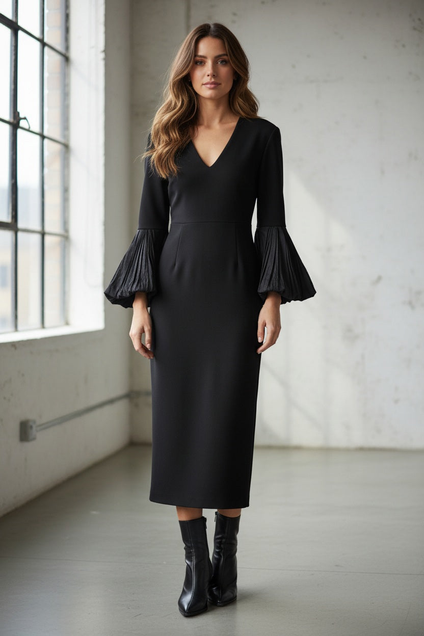 A person stands against a white wall, wearing the MEIMEIJ V Neck Midi Dress with puff sleeves and off-white pointed-toe ankle boots. Their straight dark hair and Italian craftsmanship complete the elegant look.