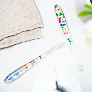 Two HAMICO - KIDS DINO TOOTHBRUSHES by HAMICO/INNOVATIVE TOOTHBRUSH, featuring unique dinosaur designs, sit on a white countertop next to a beige towel. A hint of a green plant is visible in the upper right corner, adding a touch of natural decor to the scene.
