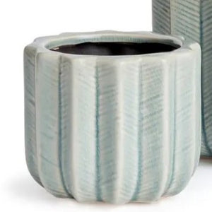 The NAPA HOME AND GARDEN - VELA POT, SMALL is a light blue ceramic decorative flower pot featuring vertical ridges and a cactus-inspired design, shown in a side view with part of another planter visible in the background.