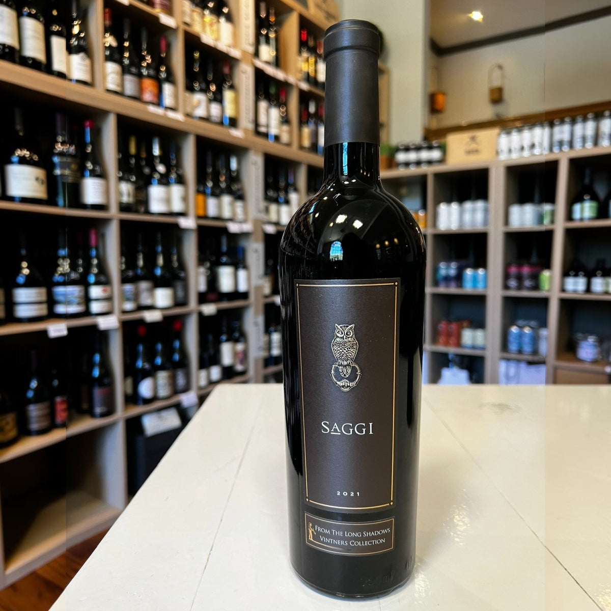A bottle of LONG SHADOWS SAGGI SANGIOVESE 2021 red wine with a black label featuring an owl illustration and the text “SAGGI 2021.”