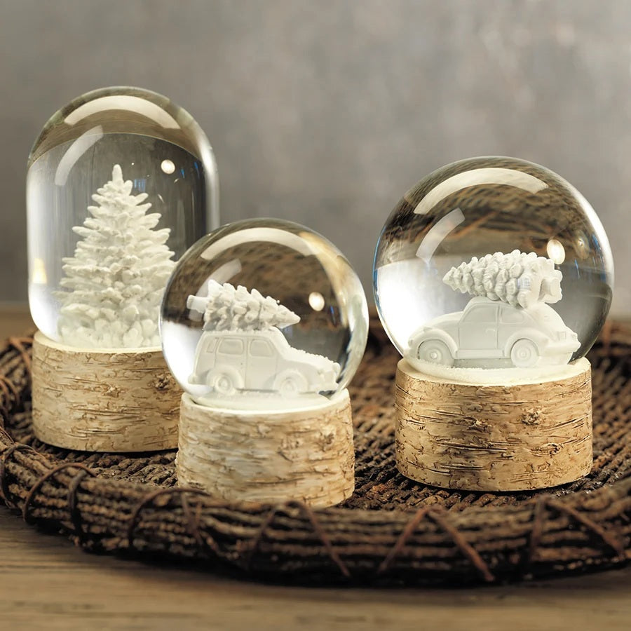 A Zodax SNOWGLOBE WITH TREE ON BIRCH BASE features a glass snow globe with a white pine tree set upon a decorative birch picture frame base.