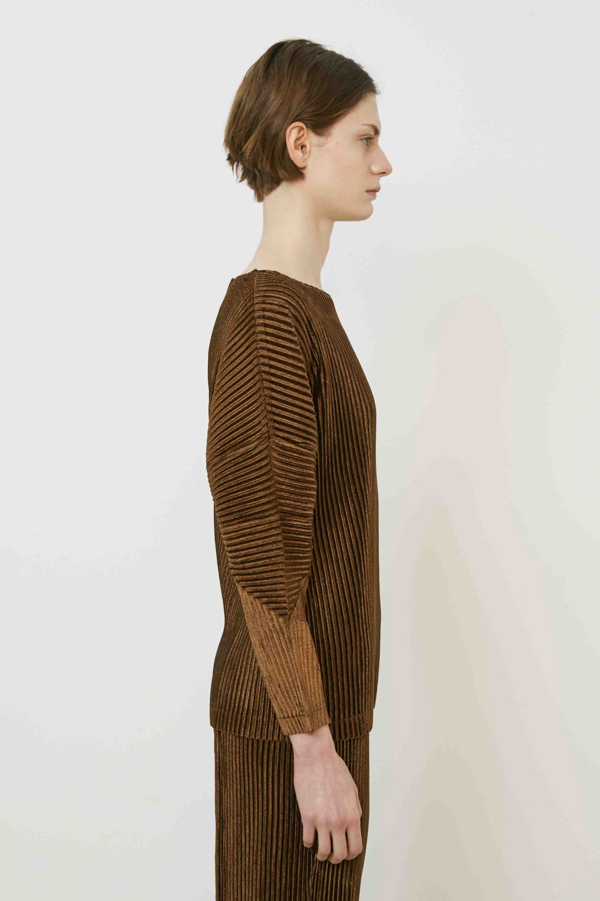 A person with short brown hair stands sideways in a MEIMEIJ - PLEAT TOP by MEIMEIJ against a plain white background, highlighting modern Italian fashion.