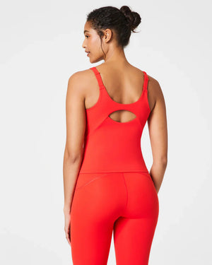 A woman wears the SPANX POWER BOOST SHELF TANK in bright pink with matching leggings, standing with her arms relaxed at her sides against a white background.
