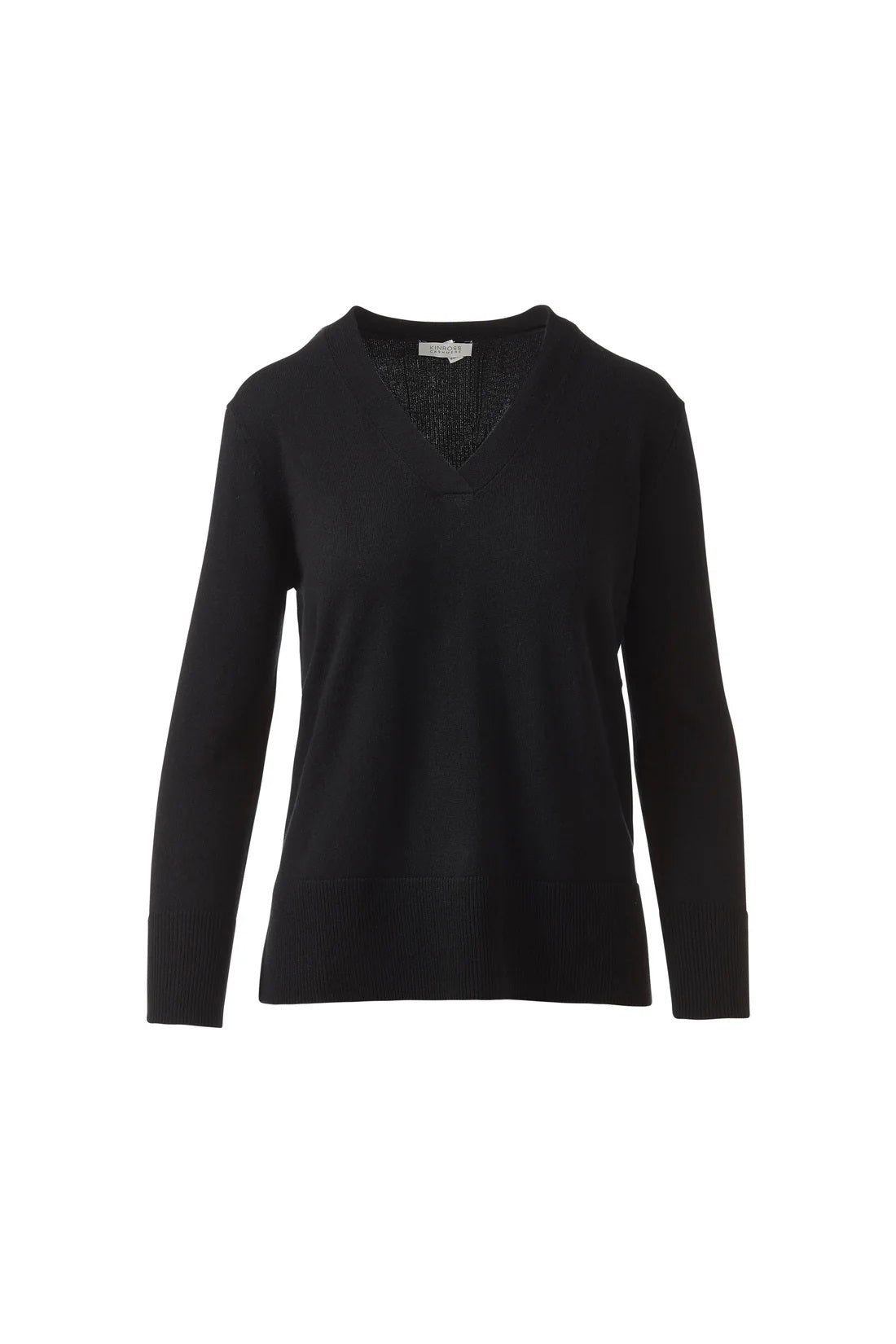 A woman with long brown hair models the KINROSS CASHMERE Hi Low Side Piped Easy Vee Neck Sweater by KINROSS, paired with blue jeans, standing against a plain white background and smiling slightly at the camera.