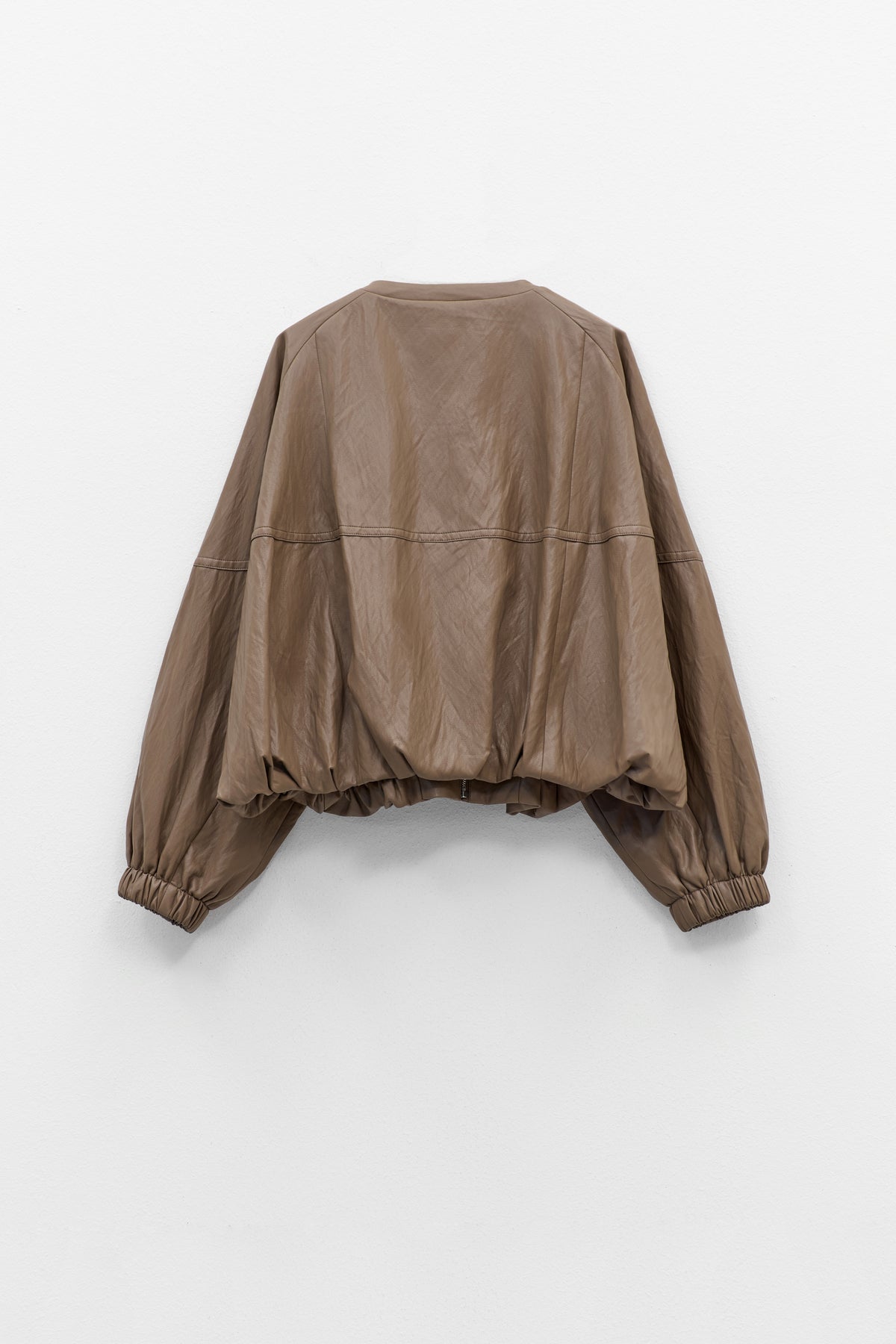The ELEH - THE MOD BOMBER JACKET by ELEH is a brown leather jacket featuring a sculptural design, front zipper, round neckline, and long oversized sleeves with gathered cuffs, shown against a plain white background.