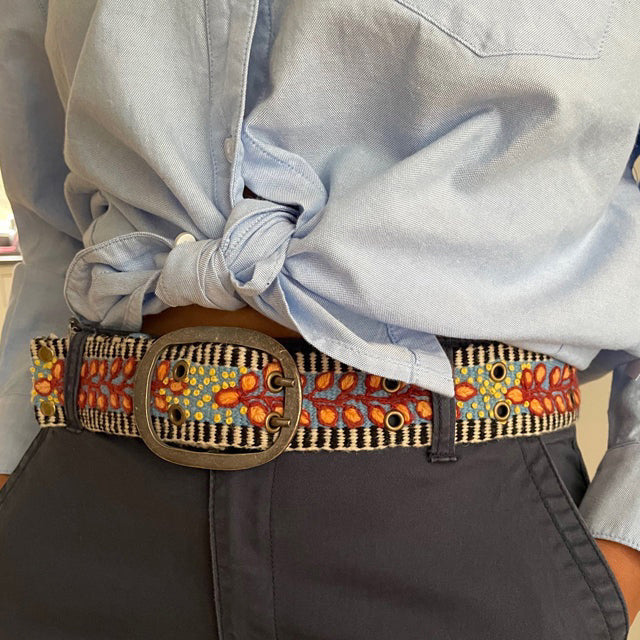 The JENNY KRAUSS - GROWING SEASON BELT by JENNY KRAUSS is a coiled, handcrafted Peruvian belt with black and white stripes, red and yellow leaf and dot embroidery, silver metal buckle, shown on a white surface.