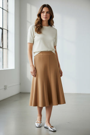 A person models the MEIMEIJ SWING SKIRT WITH LACE BACK in black, paired with silver flats, standing against a white wall. The photo is cropped at the waist and does not reveal the face.