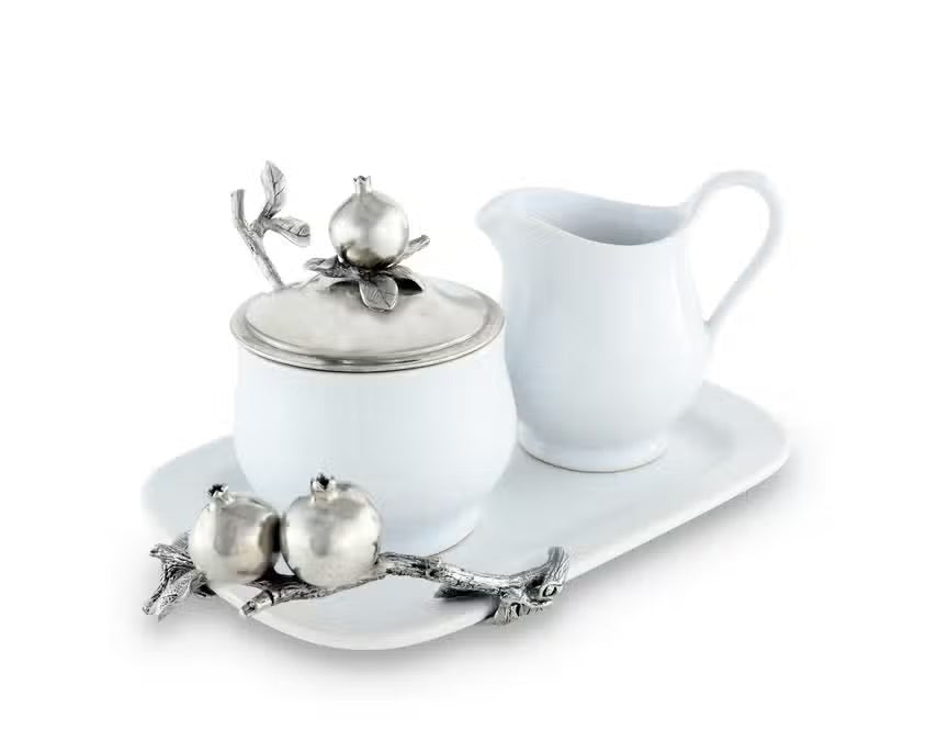 The VAGABOND HOUSE POMEGRANITE CREAMER SET includes a white ceramic sugar bowl with a metallic lid featuring pewter pomegranates, a matching cream pitcher, and a silver spoon with branch-like handle and pomegranate accents on a rectangular tray.