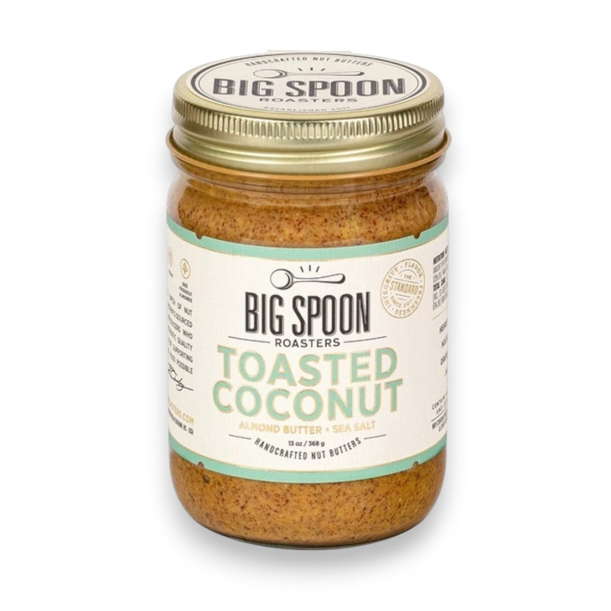 A jar of BIG SPOON ROASTERS' Toasted Coconut Almond Butter features a gold lid with a white and green label by the brand. Made with Heirloom Mission Almonds, it contains organic coconut nectar blended into light brown textured almond butter.