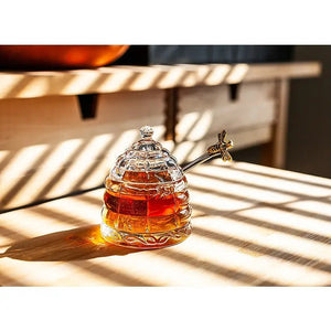 ABBOTT BEEHIVE HONEY POT WITH LID, a clear glass beehive-shaped pot with a matching lid and a silver honey dipper.