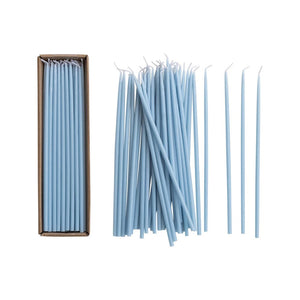 A set of CREATIVE COOP UNSCENTED THIN TAPER CANDLES in light blue, featuring white wicks, are shown arranged in a box and scattered outside it against a white background.