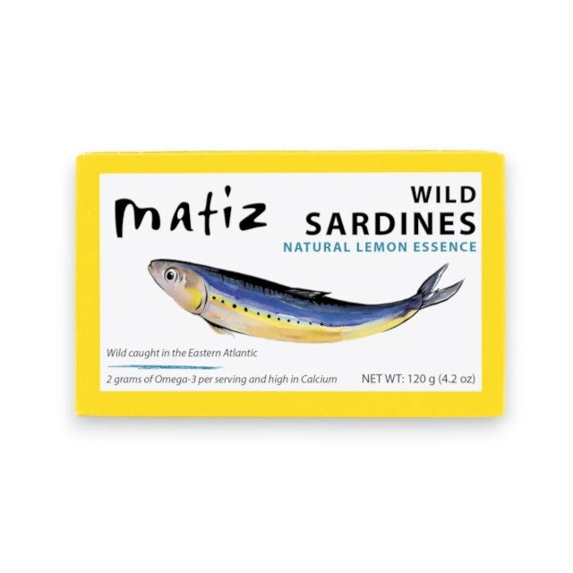 A yellow box of MATIZ ESPANA MATIZ - SARDINES WITH LEMON ESSENCE, featuring an illustration of a sardine along with product details such as weight and nutritional information. These wild-caught, bone-in sardines are packed in premium Spanish olive oil and infused with natural lemon essence for exceptional flavor and quality.