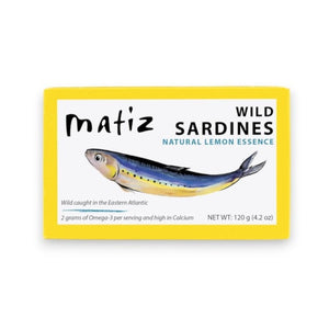A yellow box of MATIZ ESPANA MATIZ - SARDINES WITH LEMON ESSENCE, featuring an illustration of a sardine along with product details such as weight and nutritional information. These wild-caught, bone-in sardines are packed in premium Spanish olive oil and infused with natural lemon essence for exceptional flavor and quality.