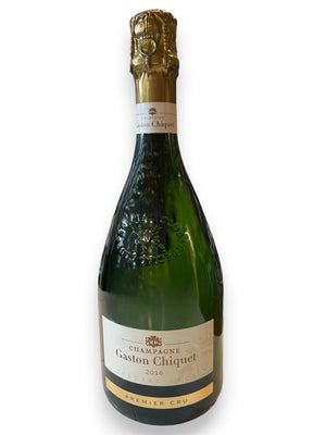 A bottle of GASTON CHIQUET SPECIAL CLUB 2016 from WINE: BORDEAUX FINE & RARE/A-VIN-GARDE sits on a white counter, displayed in front of shelves filled with assorted wine bottles in a store.