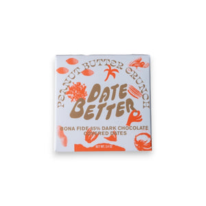 A white "DATE BETTER - PEANUT BUTTER CRUNCH COVERED DATES" package from DATE BETTER SNACKS rests on marble, cacao nibs and nuts spilling out. Orange text and illustrations adorn the packaging, adding charm to the scene.