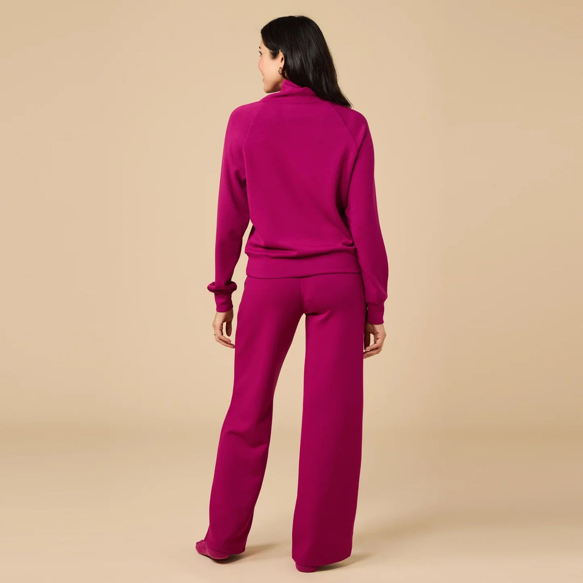 A woman seen from behind wearing the fuchsia SOFTIES - DREAMTECH COWL NECK WITH PLEATED PANT set featuring a long-sleeved cowl neck top and matching pleated pants.