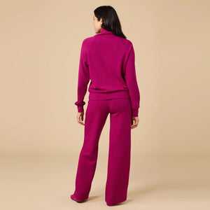 A woman seen from behind wearing the fuchsia SOFTIES - DREAMTECH COWL NECK WITH PLEATED PANT set featuring a long-sleeved cowl neck top and matching pleated pants.