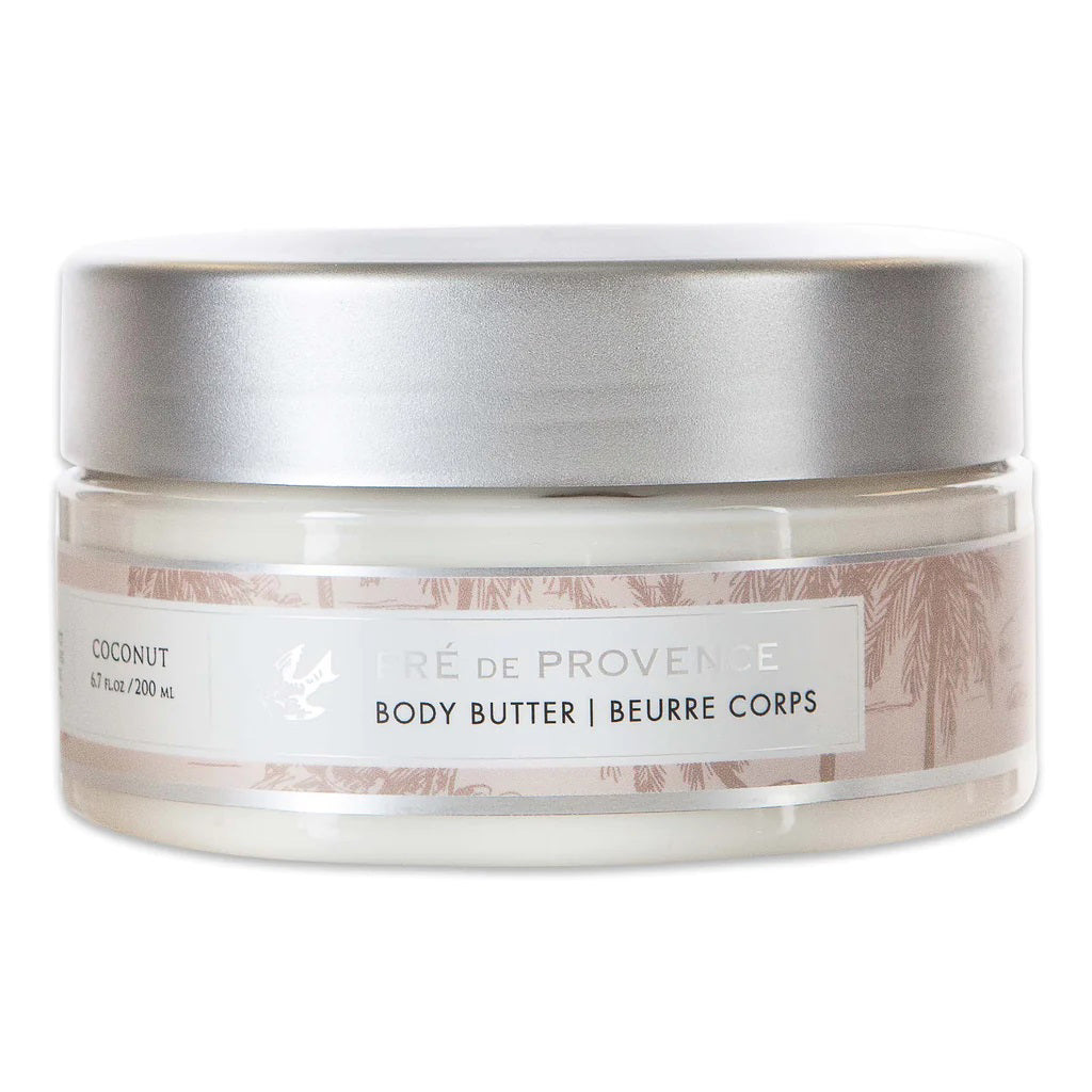 A clear plastic jar with a silver lid containing European Soaps, LLC Body Butter - Coconut, enriched with shea butter. The label displays &quot;Coconut&quot; and &quot;Body Butter | Beurre Corps,&quot; along with an illustration of coconut trees. The jar holds 6.7 fl oz (200 mL) of body butter to moisturize your skin.