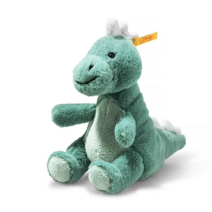 A green plush STEIFF - Joshi baby T-Rex soft plush toy, featuring a lighter green belly and white spikes along its back. Sitting upright with a tag attached to its ear, this delightful addition from the STEIFF collection truly stands as the king of the dinosaurs.