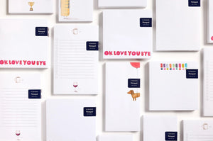 The E. FRANCES - NOTEPAD HOTDOG HIGH by E. FRANCES PAPER features a brown dachshund tied to a red heart balloon on a white background—ideal for pet lovers' stationery and proudly made in the USA.