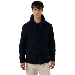A young person with short dark hair wears the HARTFORD - Sherpa Utility Jacket in Navy by HARTFORD over a black shirt, looking directly at the camera against a plain light background. This warm sherpa layer brings both comfort and style to casual menswear.