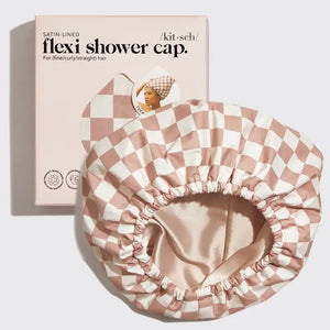 The KITSCH - SATIN LINED FLEXI SHOWER CAP, featuring a checkered pink and white design, is waterproof with satin lining and comes with adjustable closure for various hair types, as shown on its packaging.