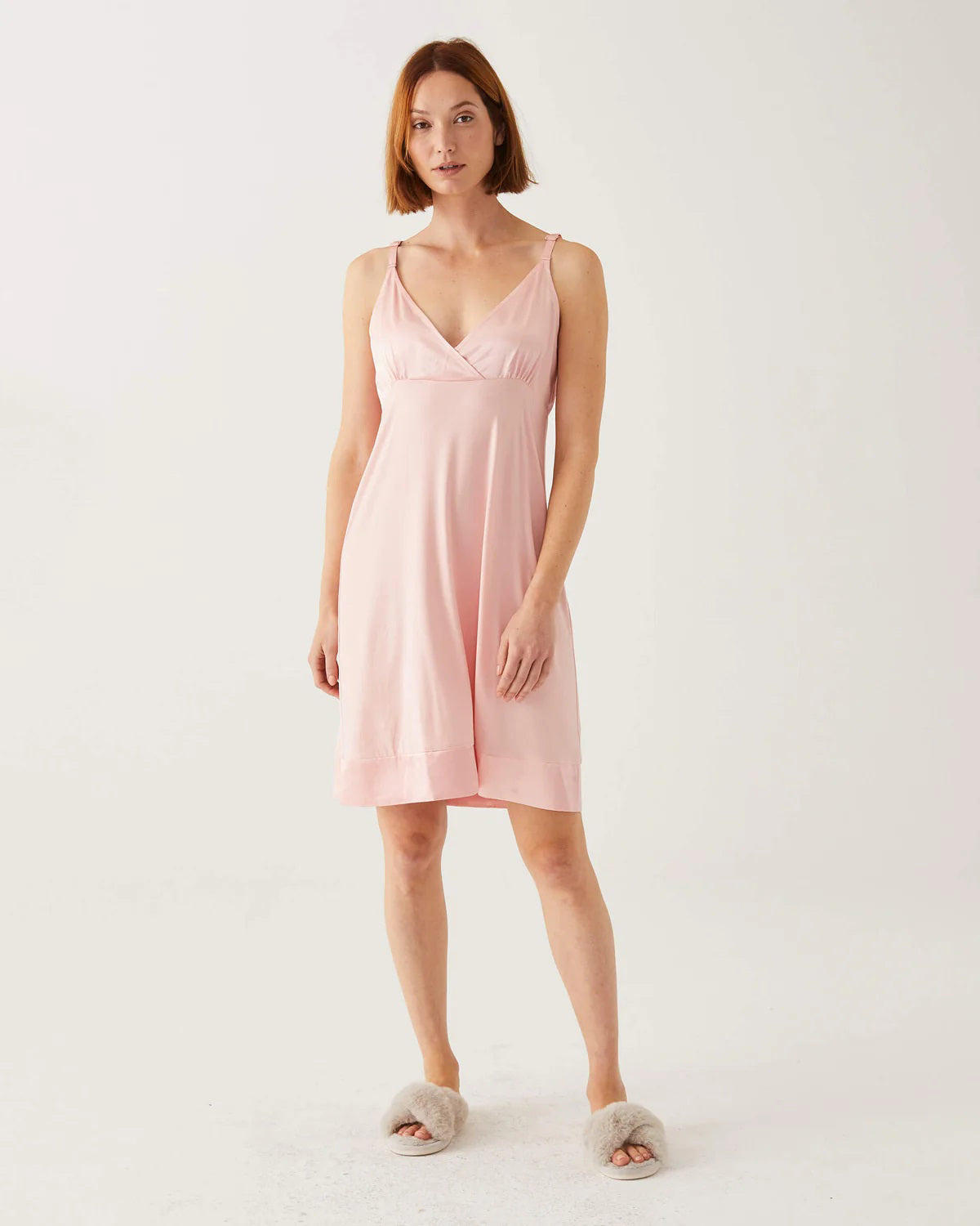 A woman stands against a white background wearing the MERSEA MOON DANCER PAJAMA DRESS in light pink with gray fuzzy slippers. With her short hair and relaxed look, it&#39;s perfect for cozy wedding pajamas or as a bride-to-be gift.