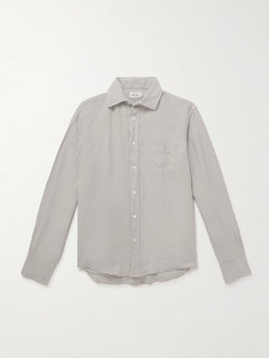 A person wears the HARTFORD - PAUL Linen Shirt in Army over a white tee and navy blue pants, standing against a plain light background.