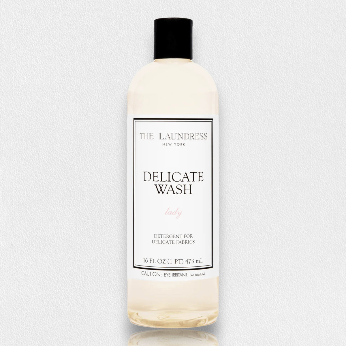 A bottle of THE LAUNDRESS - DELICATE WASH 16OZ for lady clothing is centered against a plain background. The label on the front reads &quot;THE LAUNDRESS New York, Delicate Wash, lady, Detergent for Delicate Fabrics, 16 fl oz (1 pt) 473 ml.&quot; This gentle wash with bio-based ingredients features a black cap.