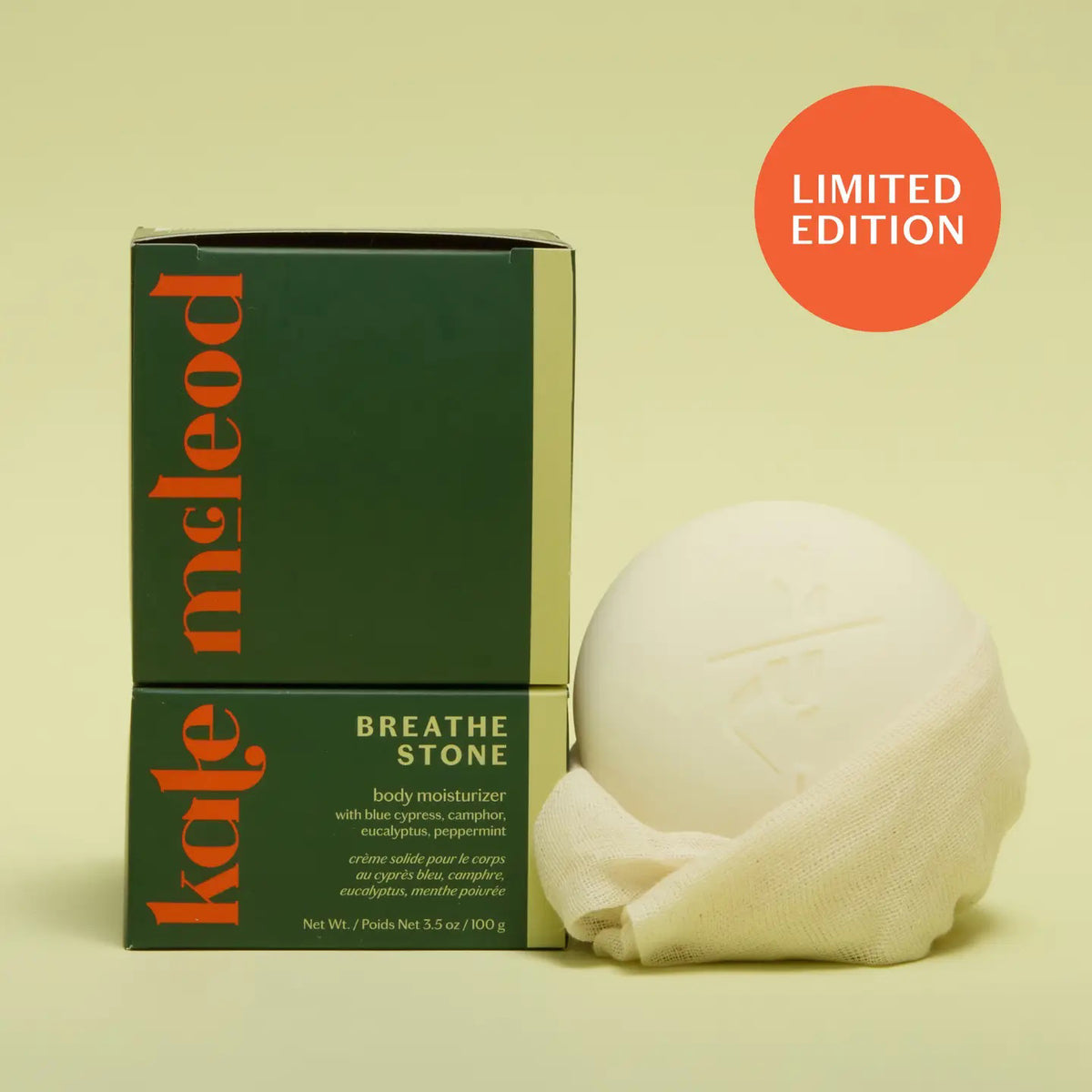 The KATE MCLEOD BREATHE STONE | SOOTHING CHEST RUB, a round white moisturizer stone with eucalyptus peppermint, is shown partially wrapped in cloth next to its green and orange box. A "LIMITED EDITION" red circle appears above on a pale yellow background.