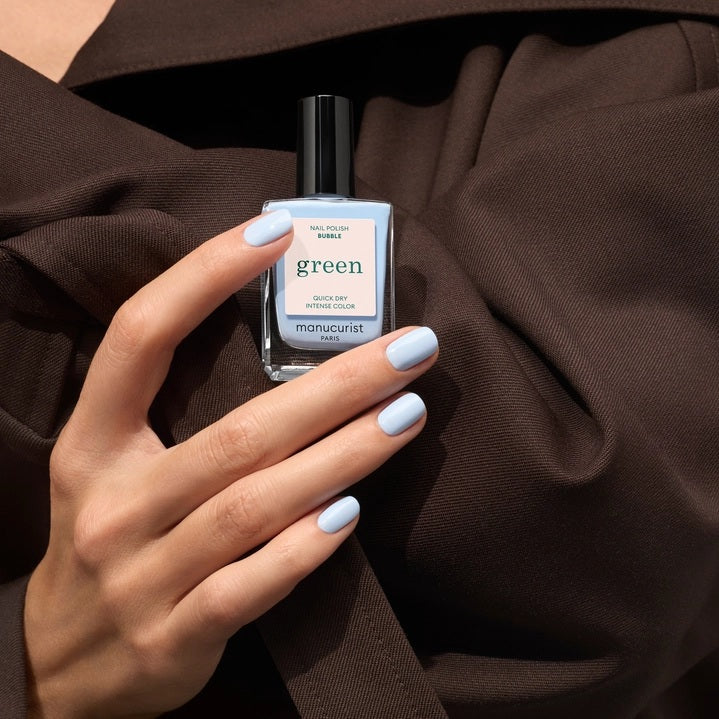 A bottle of MANUCURIST - GREEN™ Nail Polish in Bubble by MANUCURIST INC, featuring a blue and cream label with “Quick Dry Intense Color” and a black cap.
