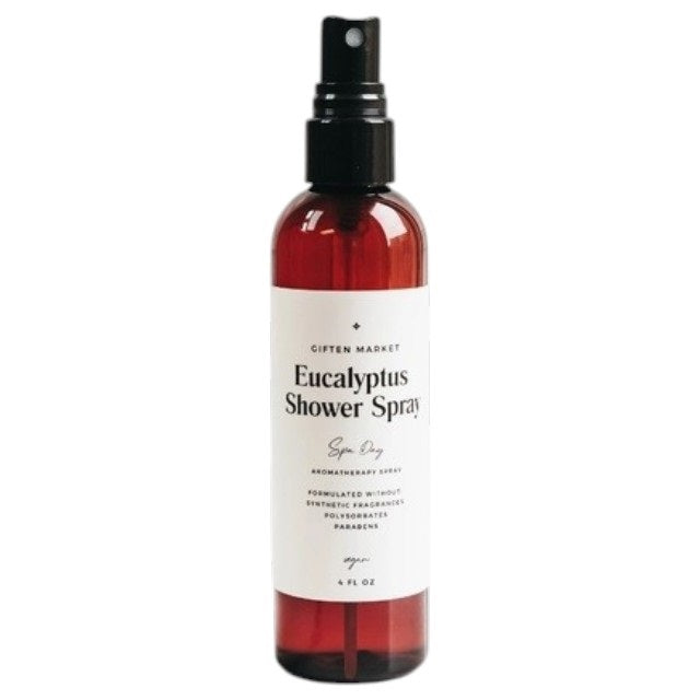 A hand holds a brown spray bottle labeled “SPA DAY EUCALYPTUS SHOWER SPRAY” by GIFTEN MARKET—an uplifting eucalyptus aromatherapy mist—set against a black showerhead and white marble shower wall, ideal for transforming your shower into a spa-like escape at home.
