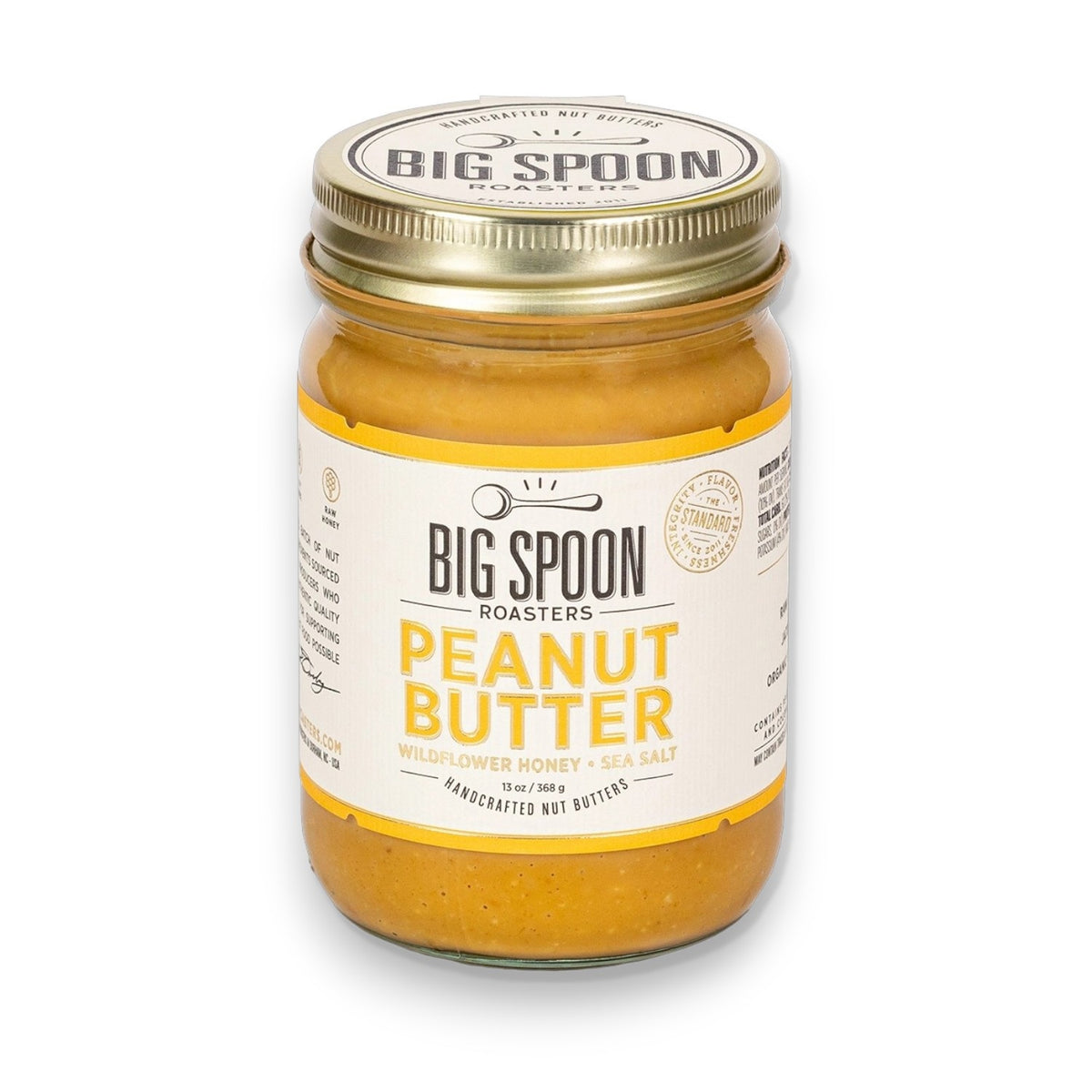 A glass jar of BIG SPOON ROASTERS Peanut Wildflower Honey Nut Butter, made with fresh-roasted peanuts, wildflower honey, and sea salt, featuring a gold lid and a white and yellow label.