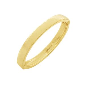 The CAPUCINE DE WULF - CLEOPATRA OVAL HINGED BANGLE SMALL/MEDIUM showcases a gleaming 18K gold plated finish with a subtly textured, hammered surface. This bangle exudes modern elegance through its simplistic, smooth oval design and reflective surface that enhances its sophisticated allure.