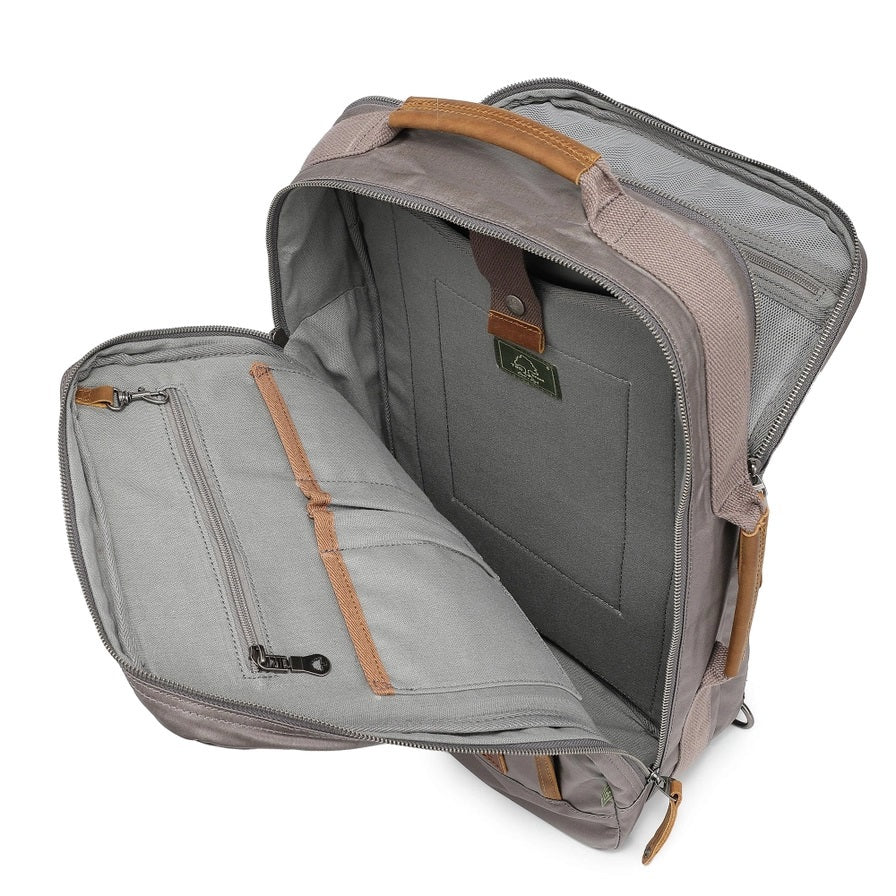 A close-up of the TSD BRAND - MADRONE Coated Canvas Backpack in Grey shows its brown leather accents and an unzipped front pocket with a black wallet partially visible inside.