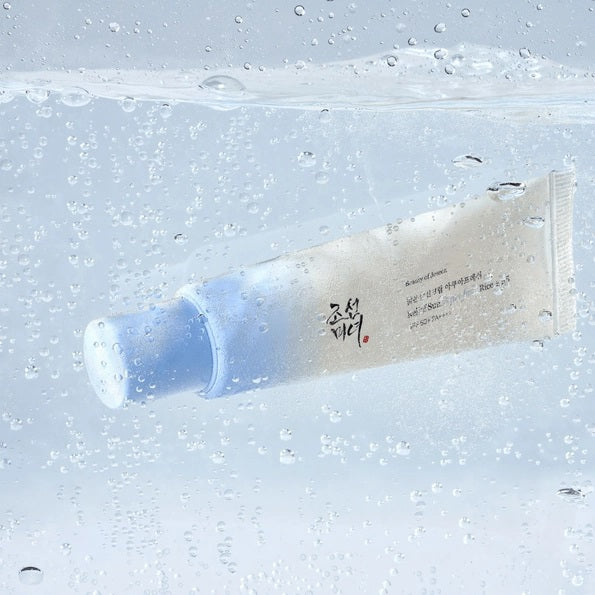 A tube of KOSMIC KBEAUTY SKINCARE BEAUTY OF JOSEON - RELIEF SUN SUNSCREEN, AQUA FRESH SPF 50+ is positioned on and next to four ice cubes containing embedded flowers, set against a crisp white background.