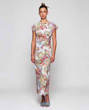 A woman stands with her back to the camera in a MIRTO 1956 PAISLEY PRINTED MIDI DRESS, featuring short sleeves, paired with light blue low-heeled shoes. Her hair is styled in a neat bun, set against a plain white background.