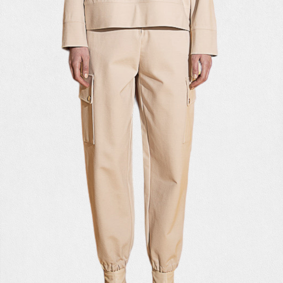 Someone dressed in MEIMEIJ - JOGGER PANT, showcasing patch pockets and elastic cuffs in beige. The jogger pant is paired with a beige top against a plain white background.