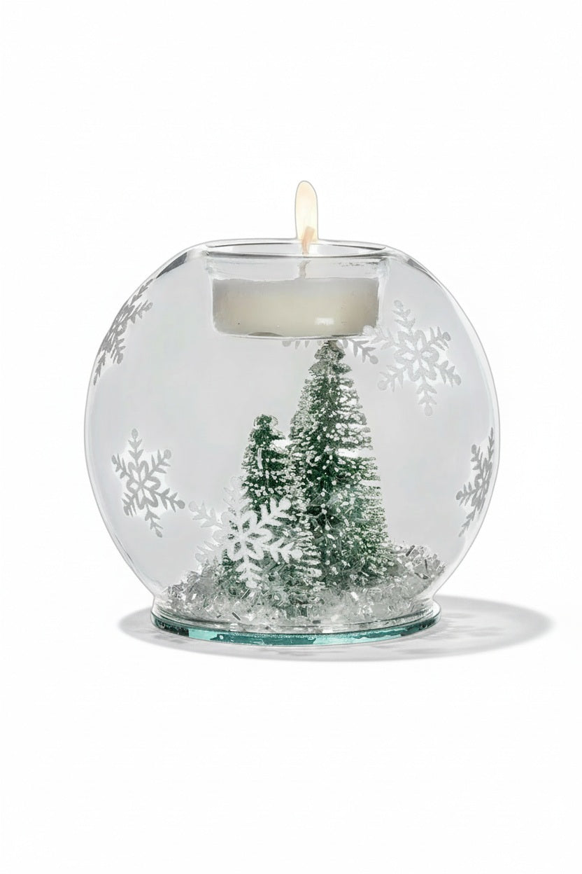 ABBOTT BRUSH TREE AND SNOW BALL VOTIVE featuring a clear glass globe with two small evergreen trees and faux snow inside, snowflake patterns on the exterior, and a lit tea light candle on top.