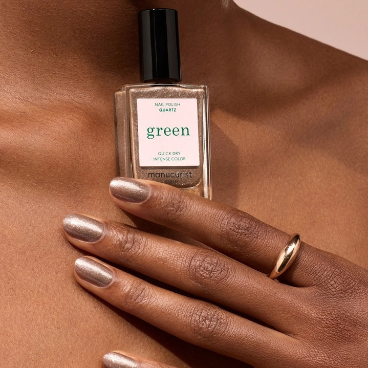A close-up of a brush spreading MANUCURIST - GREEN™ NAIL POLISH IN QUARTZ by MANUCURIST INC, showcasing its shimmery, metallic brown vegan formula with visible sparkles and swirling patterns.