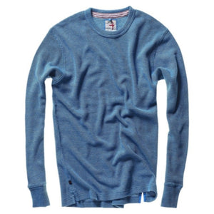 Close-up of the RELWEN - BI-WAFFLE CREW IN FRENCH BLUE, a textured light blue sweater with a vintage outdoor shirt vibe, featuring a visible collar and an inner neckline label showcasing text alongside a red and white stripe design.