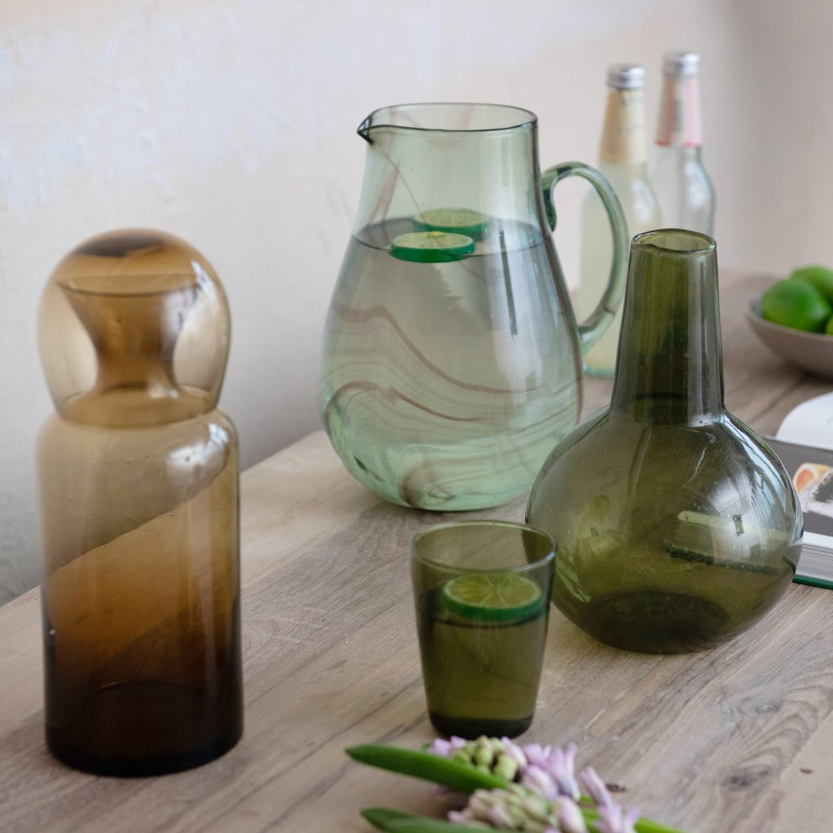 The CREATIVE COOP MARBLED GREEN AND PURPLE HAND-BLOWN RECYCLED GLASS PITCHER, featuring a curved handle and unique swirled patterns, is showcased against a plain white background.