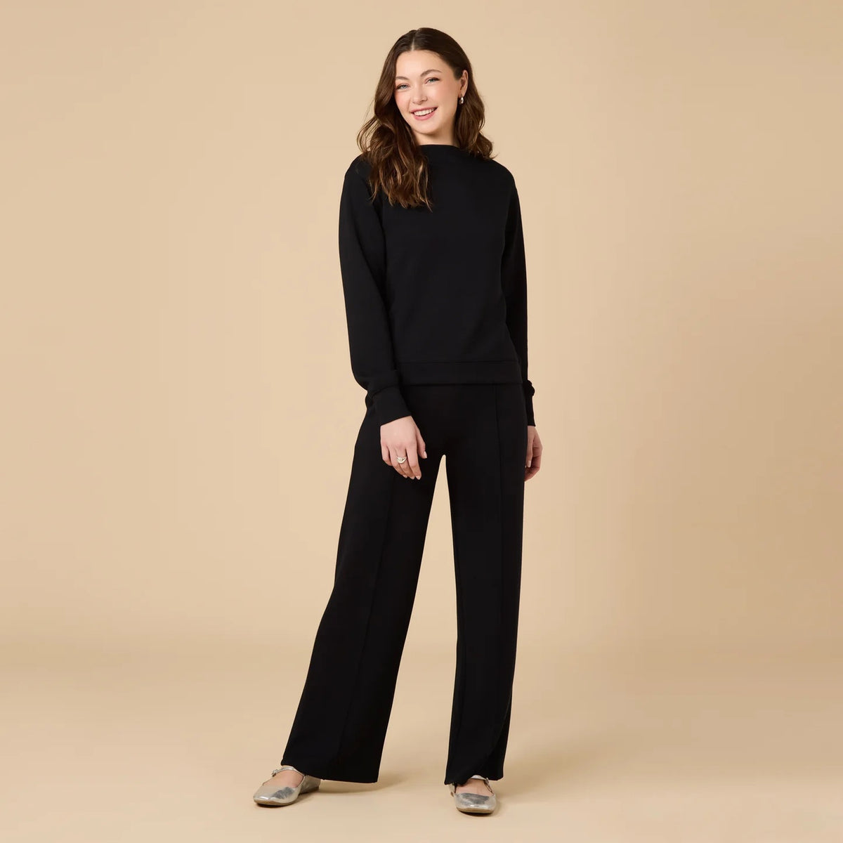 A woman wears a SOFTIES - DREAMTECH BOAT NECK WITH PINTUCK PANT SET in olive green, featuring a long-sleeve boat neck top and matching wide-leg pintuck pants.