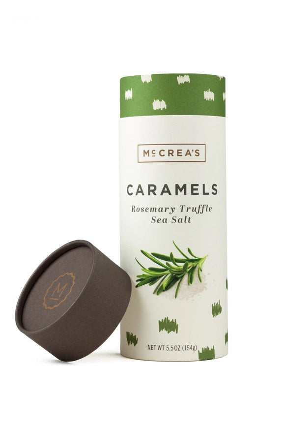 A cylindrical container of McCREA'S CANDIES ROSEMARY TRUFFLE SEA SALT CARAMELS features a green and white design with rosemary and sea salt illustrations. The brown lid is shown next to the container.