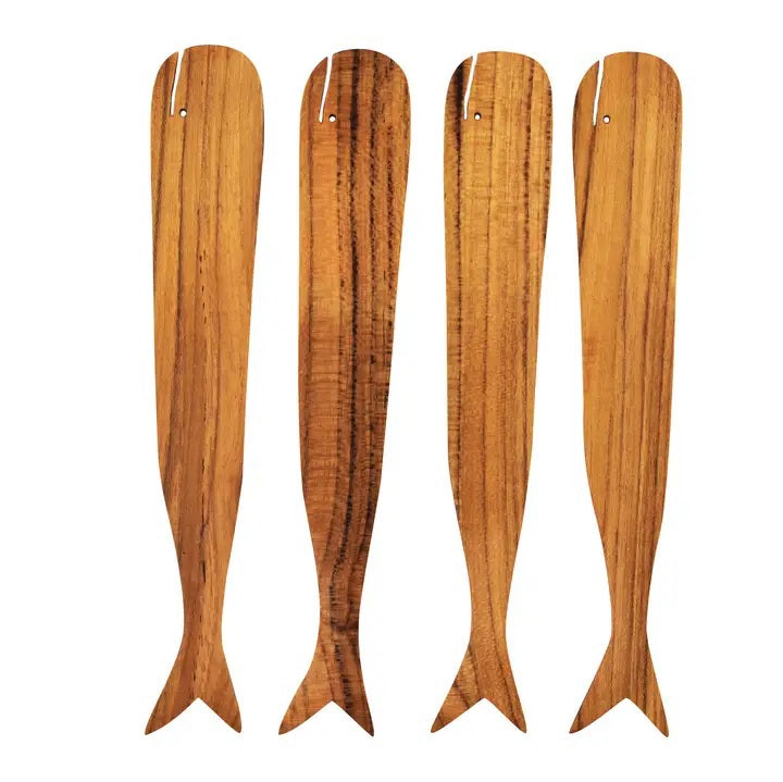 The BE HOME - TEAK WHALE SPREADERS by BE HOME, INC rest on a round white marble cutting board with a hole at the top, displayed on a wooden surface.